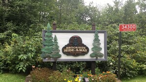 A sign for Brookside Hide-A-Way with a welcome message, surrounded by greenery and flowers. - Bayfield- Charming Condo, Jumping Off Point to Apostles (Bayfield)