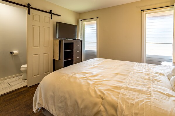 A bedroom with a large bed, a TV on a stand, a wardrobe, and a door leading to a balcony.