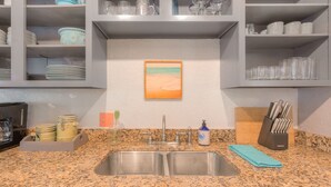 A kitchen with granite countertops, a double sink, and a painting of a beach scene. - The Beach Retreat, 3 Beds, Walk to Beach, Shops & Pier, Beach Items Included (St Augustine Beach)