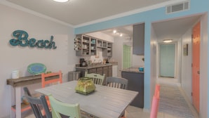 A dining area with a table and chairs, a kitchen with cabinets and a sink, and a hallway with a door. - The Beach Retreat, 3 Beds, Walk to Beach, Shops & Pier, Beach Items Included (St Augustine Beach)