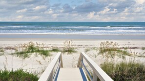 Une promenade en bois qui mène à une plage de sable où la végétation est clairsemée.