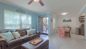 A living room with a brown leather sofa, a wooden tray with a remote, and a dining area with a table and chairs. - The Beach Retreat, 3 Beds, Walk to Beach, Shops & Pier, Beach Items Included (St Augustine Beach)