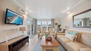 A spacious living room with a large TV, comfortable seating, and a view of the ocean. - Emerald Isle 107-On the Beach-Ground Floor (Fort Walton Beach)