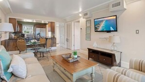 A spacious living room with a dining area, a kitchen, and a television mounted on the wall. - Emerald Isle 107-On the Beach-Ground Floor (Fort Walton Beach)