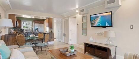 A spacious living room with a dining area, a kitchen, and a television mounted on the wall.
