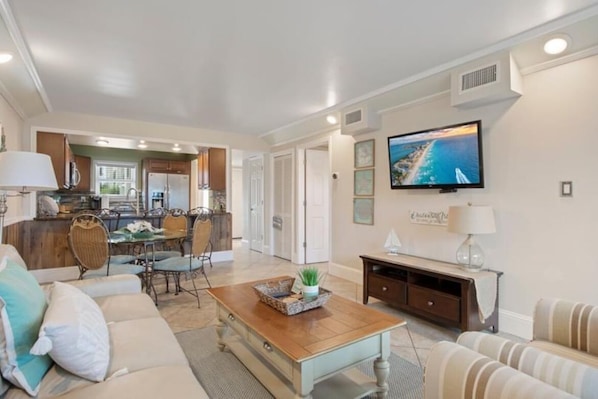 A spacious living room with a dining area, a kitchen, and a television mounted on the wall.