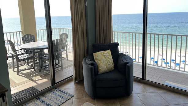 A balcony with a view of the ocean, a dining table with chairs, and a cushioned chair with a pillow. - ⛱ 803 /ON the BEACH! 🏖 (Orange Beach)
