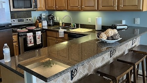 A kitchen with wooden cabinets, a granite countertop, a built-in stove, a microwave, a sink, and a hanging light fixture. - ⛱ 803 /ON the BEACH! 🏖 (Orange Beach)