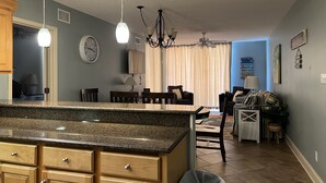 A kitchen with granite countertops, wooden cabinets, a dining area with chairs, and a chandelier. - ⛱ 803 /ON the BEACH! 🏖 (Orange Beach)