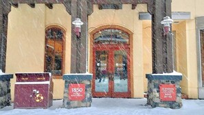 Entrada de un edificio con el suelo cubierto de nieve, dos contenedores de basura y un cartel que indica '1850 Village Road South'.
