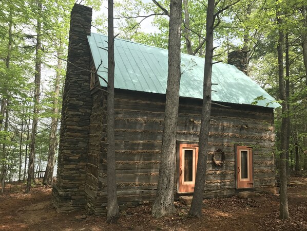 Une cabane rustique en rondins de bois, surmontée d’un toit en métal, entourée de grands arbres.