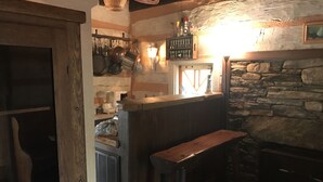 A rustic kitchen with wooden bar stools, a stone wall, and hanging pots.