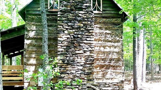 A rustic cabin with a stone facade, wooden beams, and a chimney.