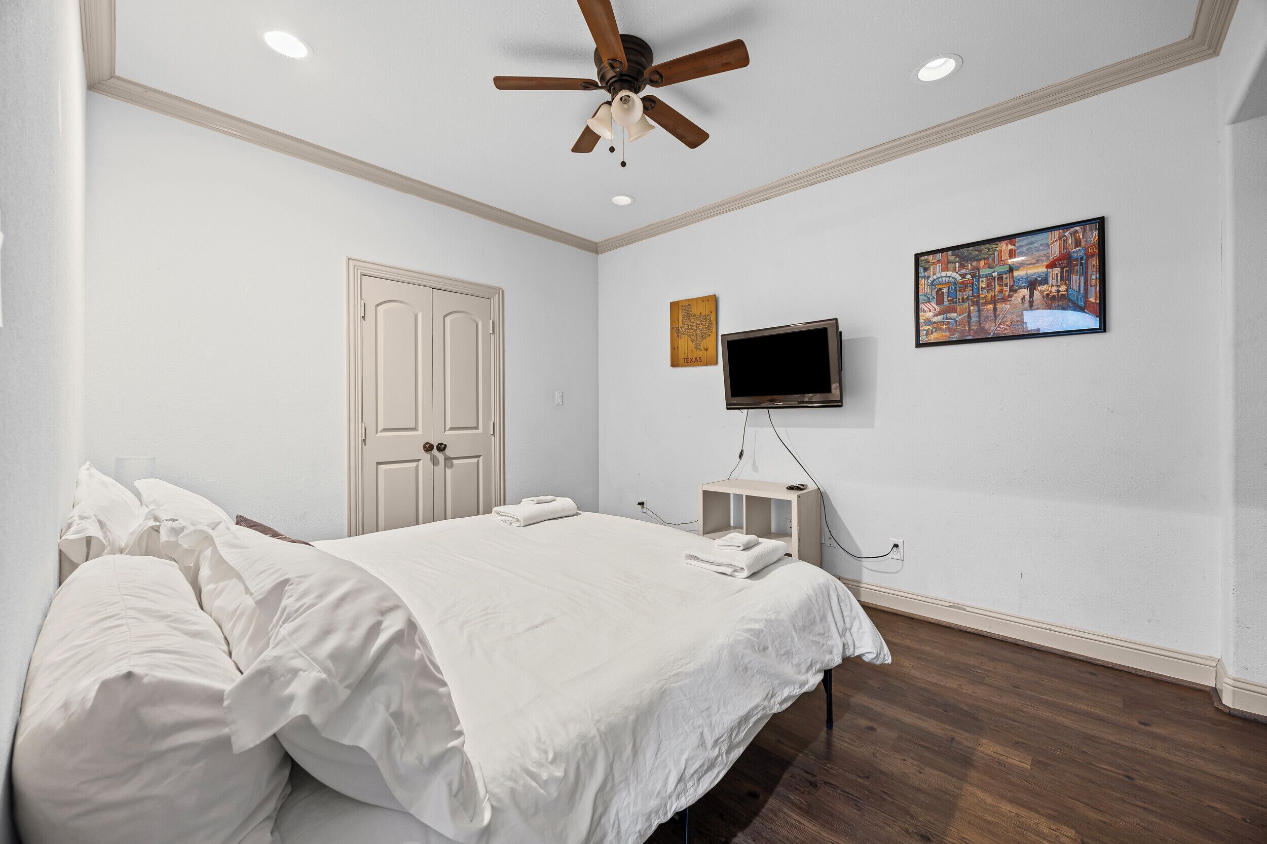 Une chambre à coucher avec un lit, un ventilateur de plafond, une télévision et une porte.