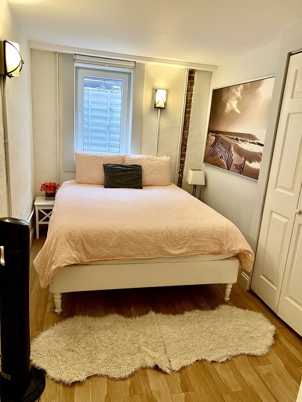 Un dormitorio con cama, ventana, lámpara de pared, cuadro y puerta.