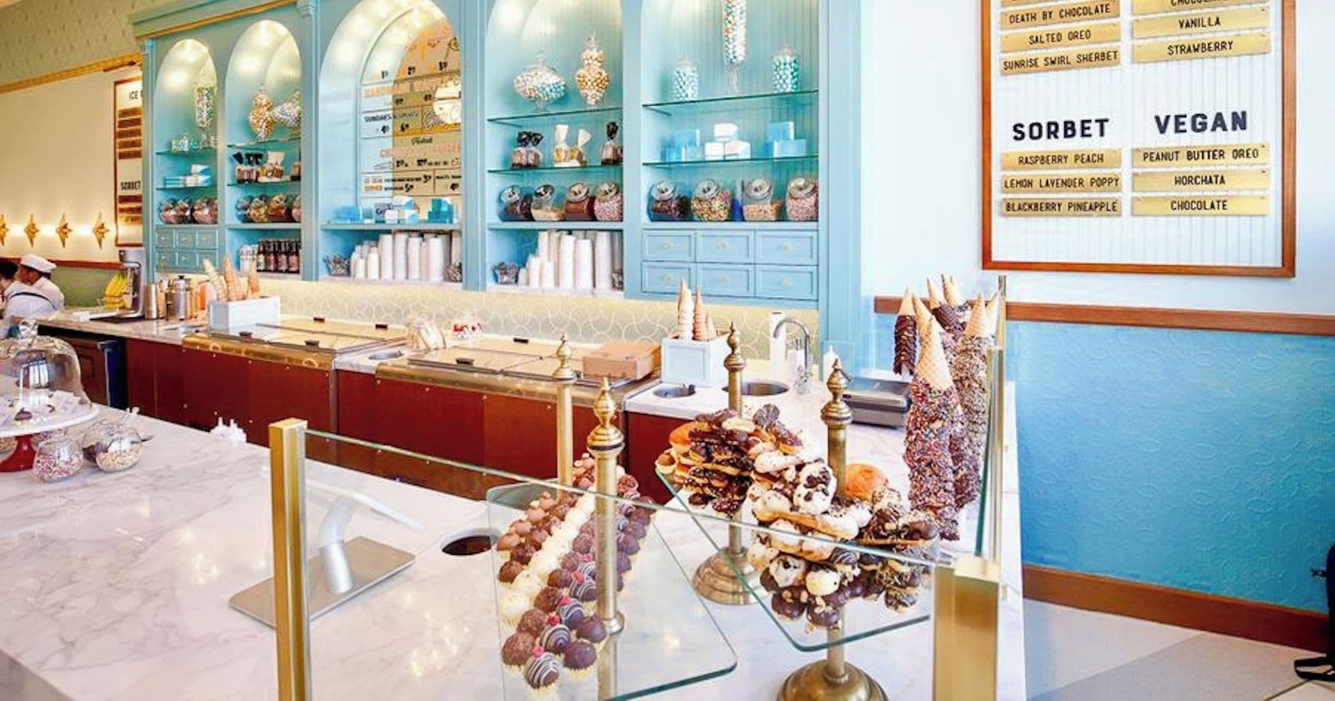 An ice cream parlor with a variety of ice cream flavors and sorbets displayed on shelves and a menu board.