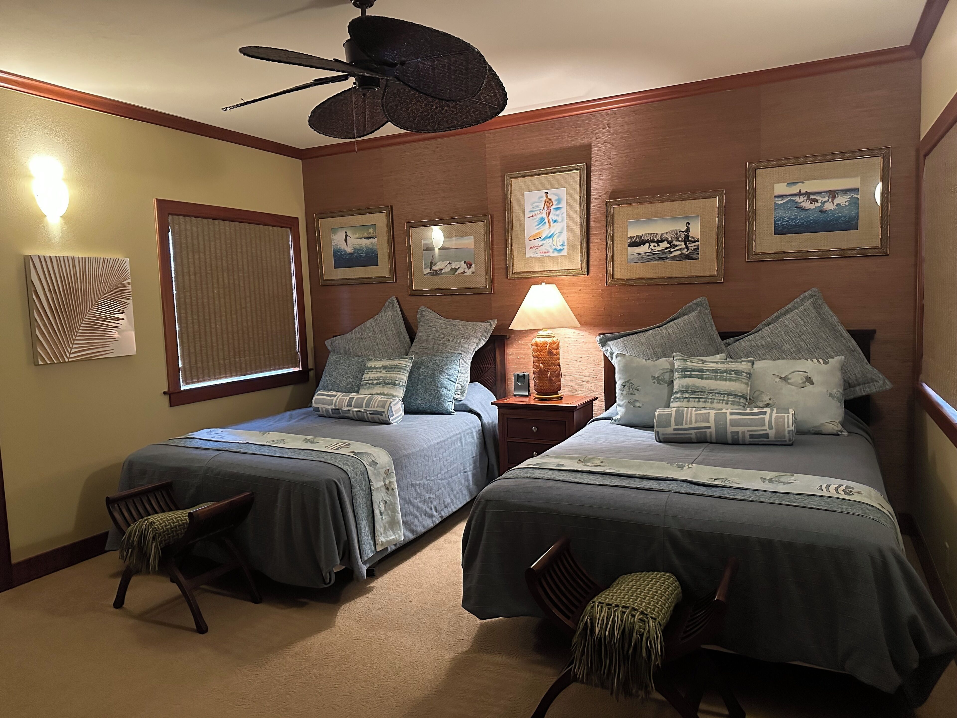Een hotelkamer met twee bedden, een plafondventilator, een lamp en ingelijste foto’s aan de muur.