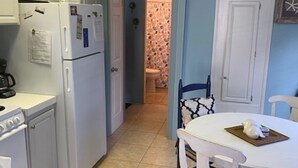 Una cuina compacta amb armaris blancs, un frigorífic, una placa de cocció i una taula de dinar amb cadires.