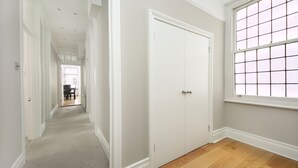 A hallway with a wooden floor, white walls, and a large window with a grid pattern. - 110 m² luxury two-bed apartment in Earls Court (London)