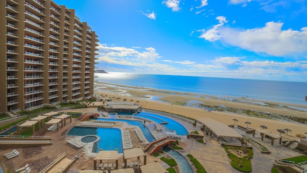 A resort with multiple swimming pools, a beach, and a high-rise building.