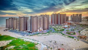 A beachfront hotel with multiple high-rise buildings, a sandy beach, and a golf course.
