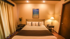 A hotel room with a large bed, a nightstand with a lamp, a painting on the wall, and a door.