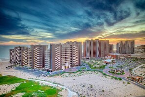 Un hotel frente a la playa con varios edificios altos, una playa arenosa y un campo de golf.