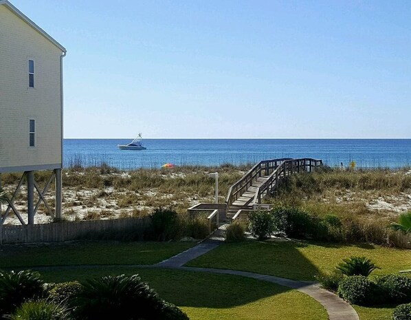 A coastal property with a wooden staircase leading to a beach, a white building, and a clear view of the ocean.