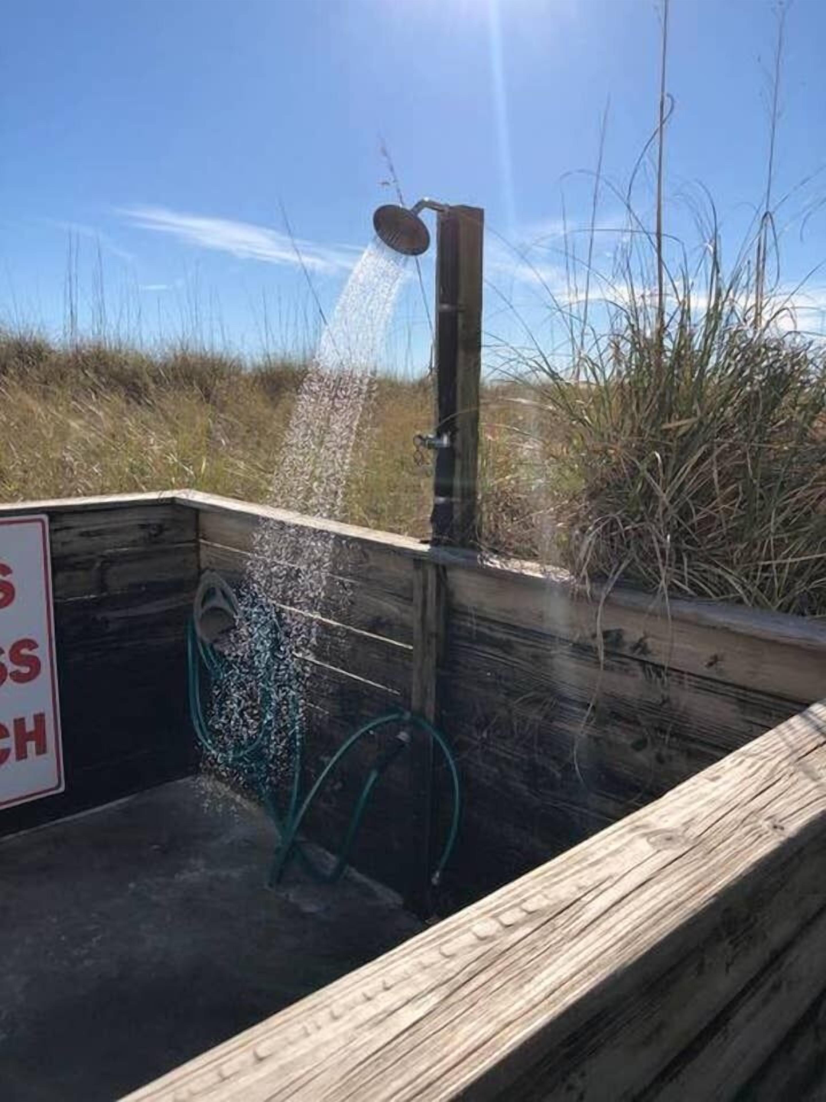 Een houten constructie met een douchekop die water spuit, omringd door hoog gras.