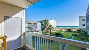 Un balcó amb vista a una platja, un jardí ajardinat i un edifici amb una escala.