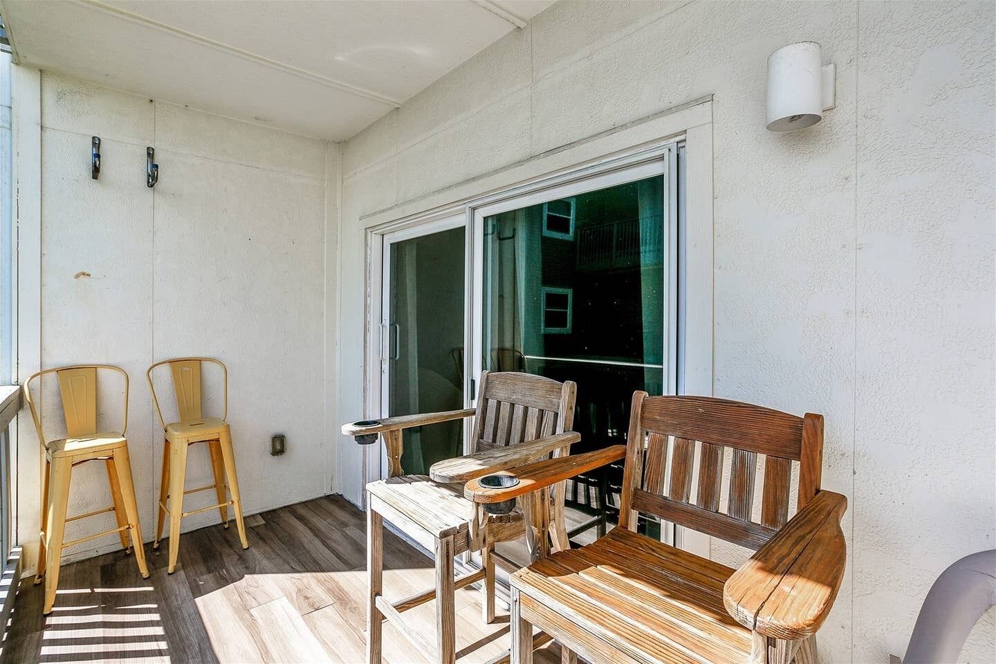 En balkon med træstole, et træbord og en skydedør i glas.