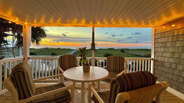 Un espace extérieur aménagé, abrité et doté de tables et de chaises, offrant une vue panoramique sur une plage et des dunes.