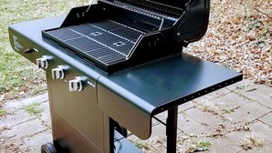 A portable barbecue grill with wheels, a side table, and a control panel.