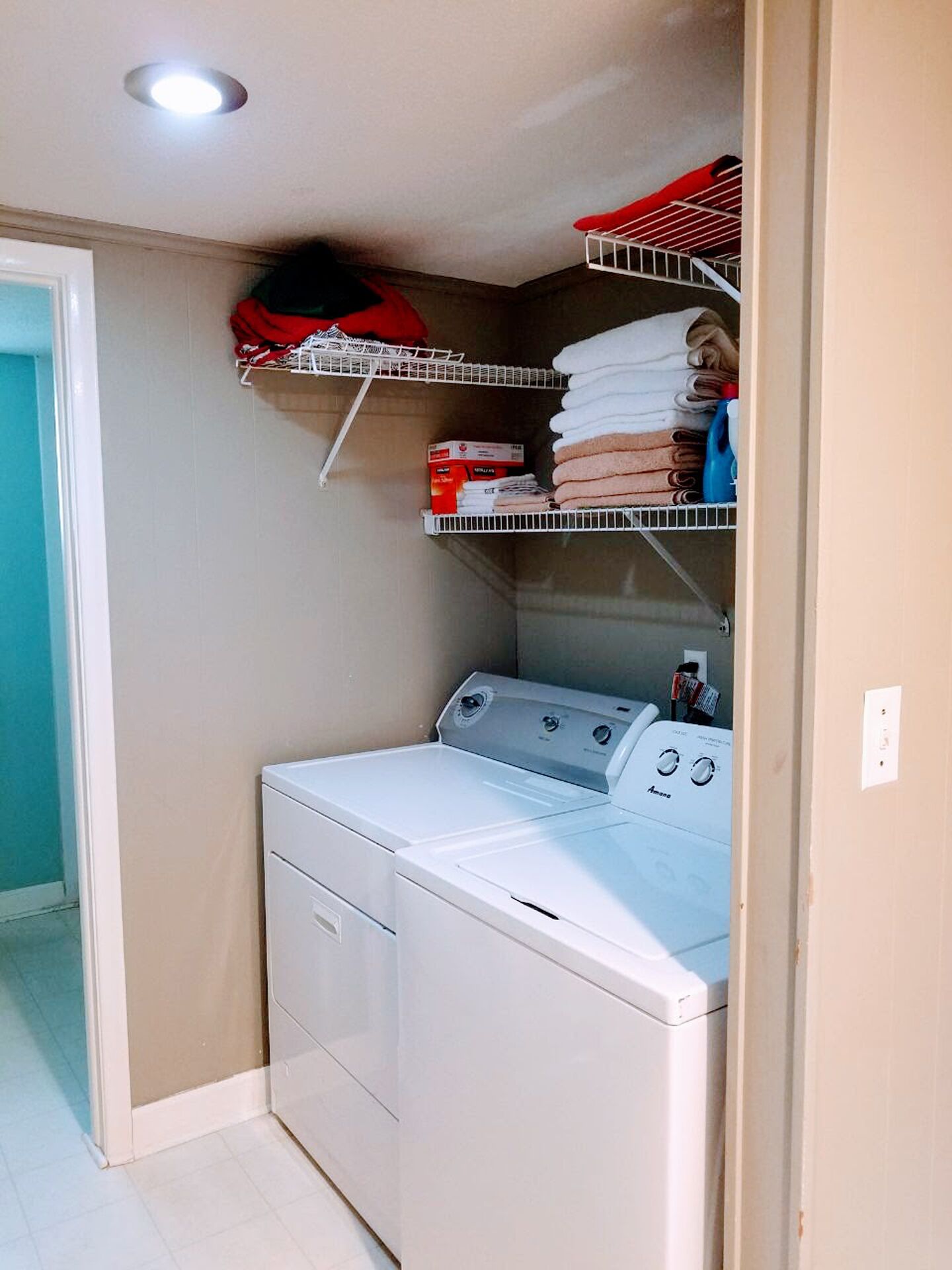 A laundry area with a front-loading washer and dryer, shelves with folded towels, and a red basket.