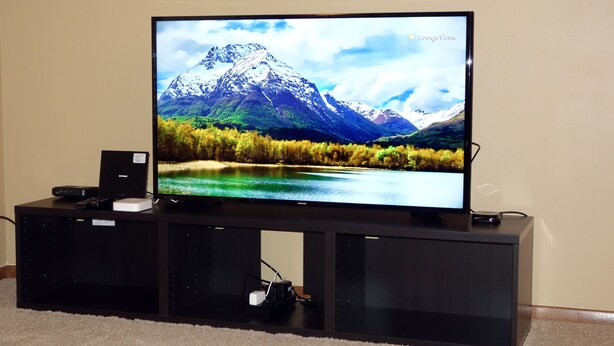 A flat-screen TV on a black entertainment unit with a remote and a speaker.