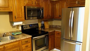 A kitchen with wooden cabinets, stainless steel appliances, a granite countertop, and a tiled floor.