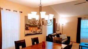 A dining area with a wooden table and chairs, a chandelier, and a large framed picture on the wall.