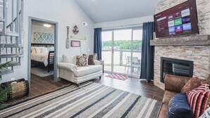 Un salón amplio con chimenea, un televisor grande montado en la pared y un balcón con vistas a los alrededores.