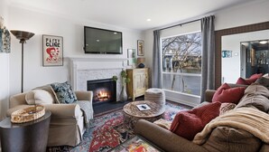A living room with a fireplace, a sofa, a coffee table, and a television mounted on the wall.