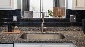 A kitchen with white cabinets, a granite countertop, a stainless steel sink, and a window with a view.