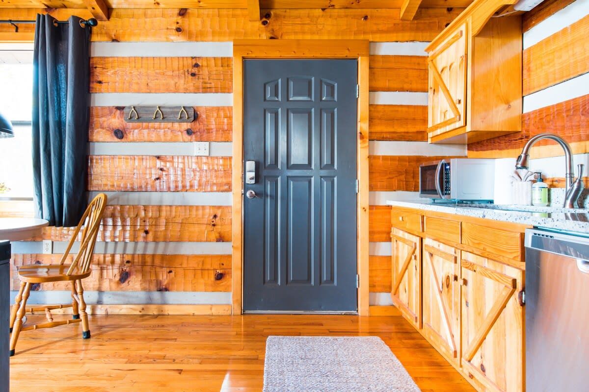 Un intérieur en bois avec une porte noire, des placards en bois, un four à micro-ondes et une chaise.