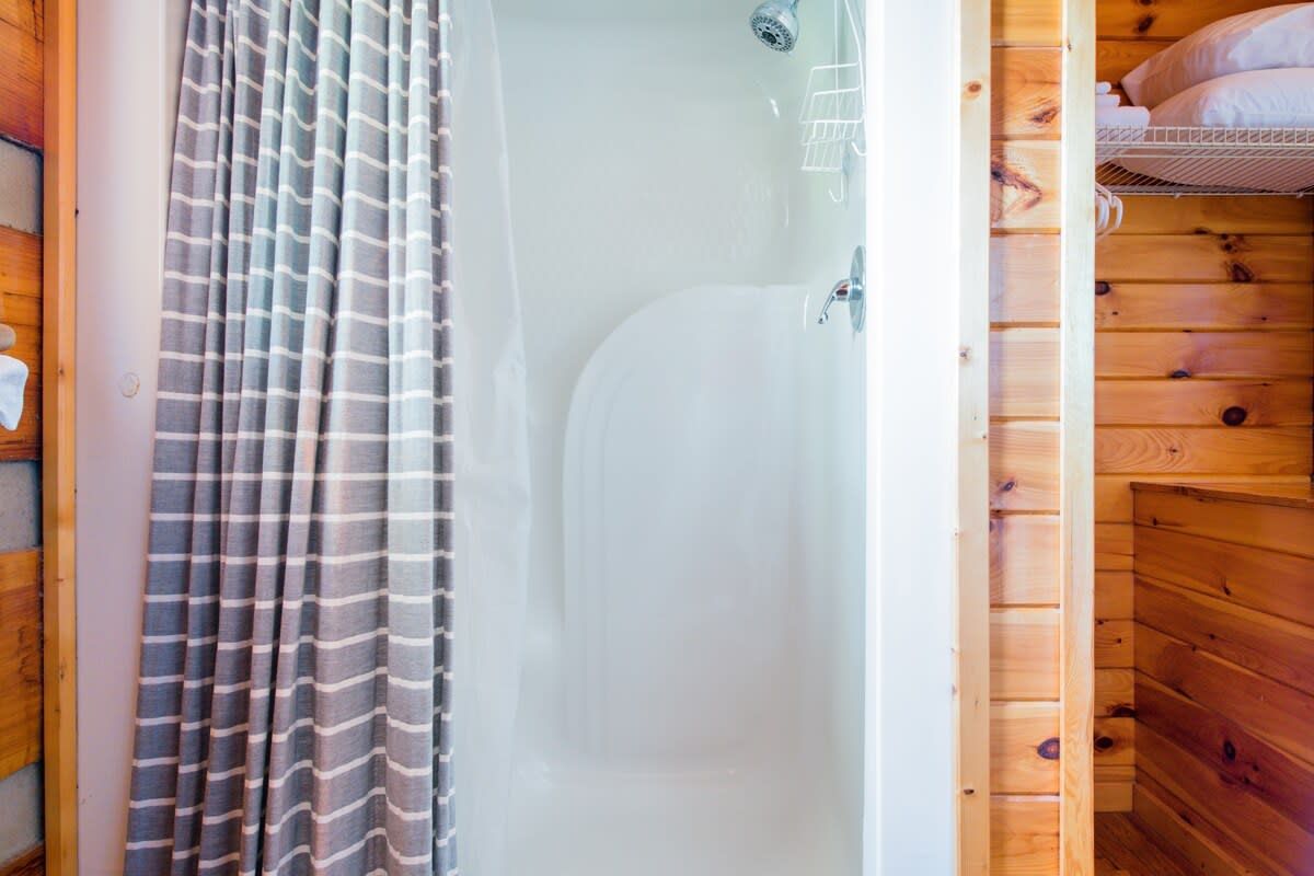 Interior de una cabaña de madera con ducha, paredes de madera y una cama con almohadas.