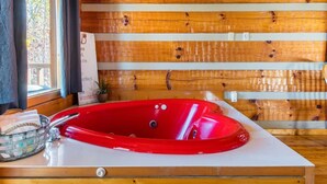 Una vasca da bagno rossa in una baita di legno, con una finestra e un cartello appeso al muro.