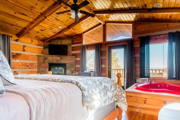 Un dormitorio tipo cabaña de madera con cama, chimenea, bañera de hidromasaje roja y balcón.