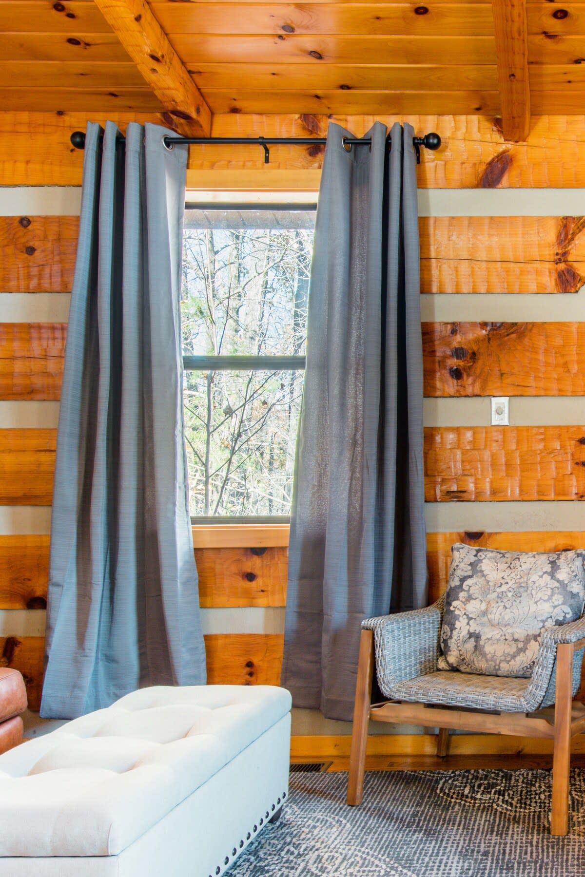 A cabin interior with a window, curtains, a chair, and a sofa.