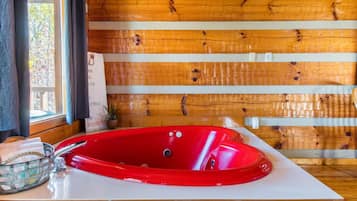 Une baignoire rouge dans une cabane en bois, avec une fenêtre et un panneau accroché au mur.