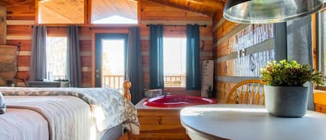 Acogedora habitación tipo cabaña con una cama, una mesa redonda, una planta en maceta y vistas al exterior a través de amplias ventanas.