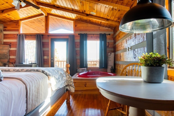 Acogedora habitación tipo cabaña con una cama, una mesa redonda, una planta en maceta y vistas al exterior a través de amplias ventanas.