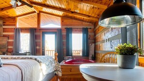 Una camera accogliente in stile baita, con soffitto in legno, un letto, un tavolo da pranzo e una finestra con tende.