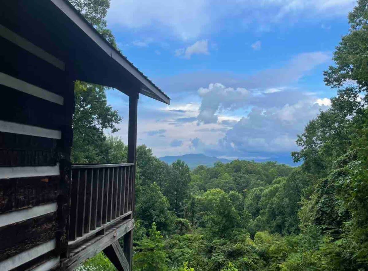 Une cabane en bois dotée d’un balcon donnant sur une forêt dense et des montagnes lointaines.